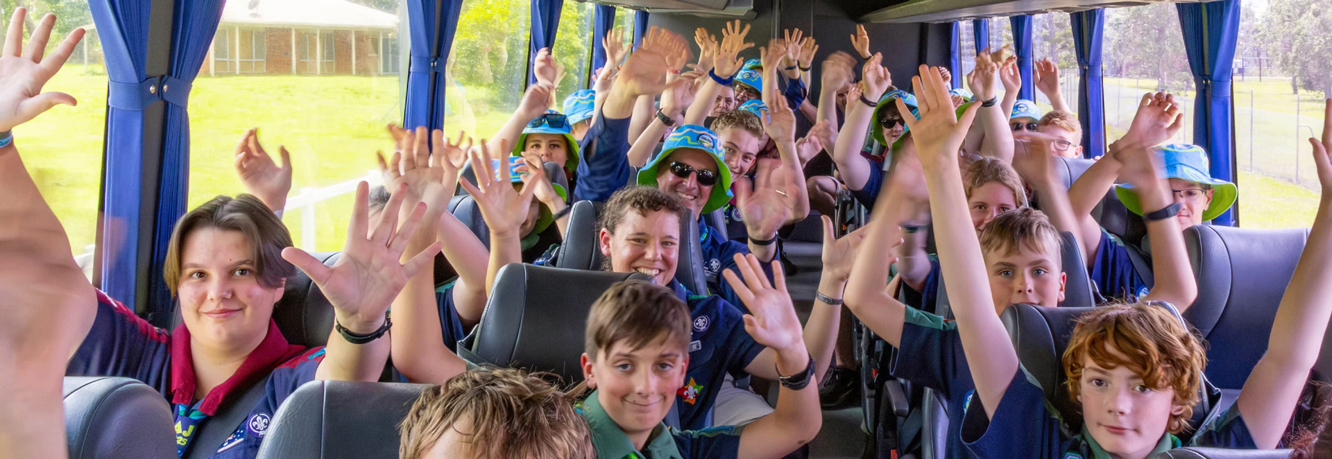 Excited Scouts on a bus waving with hands raised, ready for the Jamboree